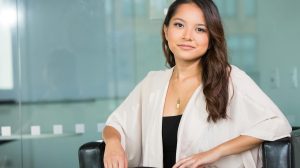 A professional Asian businesswoman sitting confidently in a modern office setting.