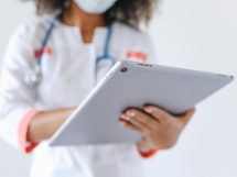 Close-up of a doctor wearing a mask using a tablet for healthcare management.