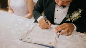 Groom signing marriage certificate with bride beside him