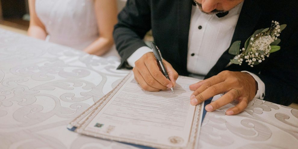 Groom signing marriage certificate with bride beside him