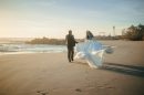 A bride and groom walk on a beach at sunset